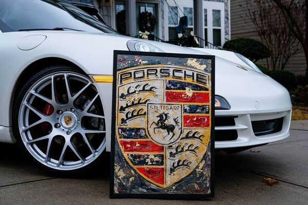 Copper-toned Porsche Crest painting displayed beside a Porsche