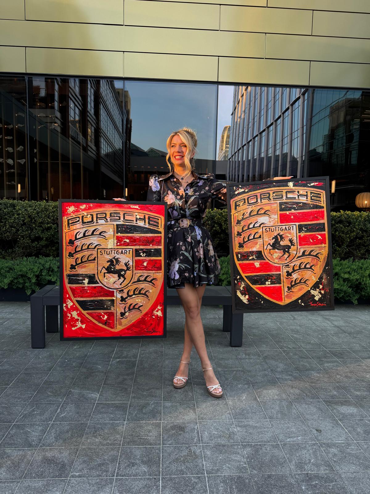 Tanja holding two Porsche Crest paintings outdoors